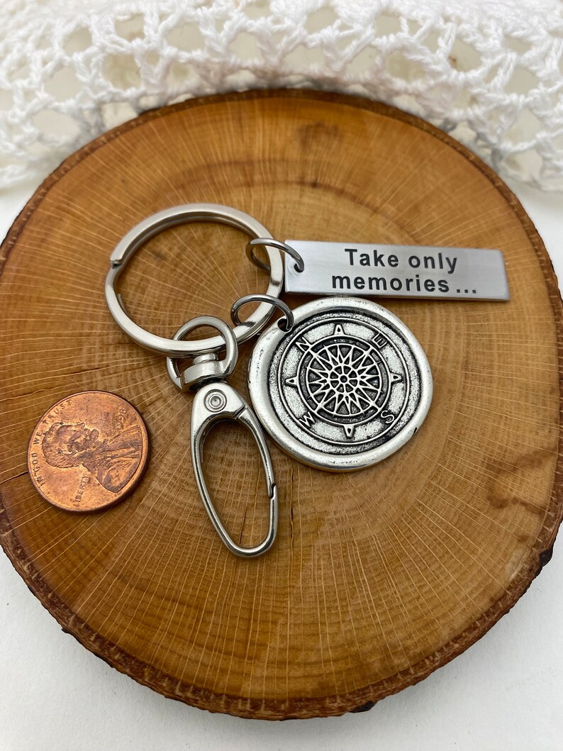 May include: Silver compass keychain with a silver tag that reads "Take only memories..." The keychain is on a wooden surface.