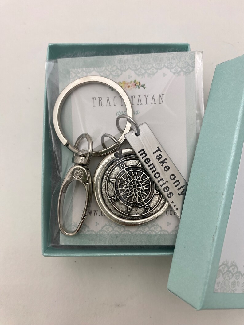 May include: Silver keychain with a compass charm and a tag that reads "Take only memories..." The keychain is in a light blue gift box with a white lace design.