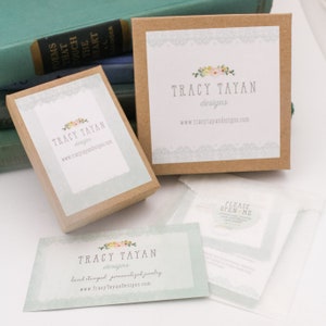 May include: A brown box with a white label that says "Tracy Tayan designs" and a website address. The box is sitting on a white surface. There is a smaller brown box with a similar label in the background.