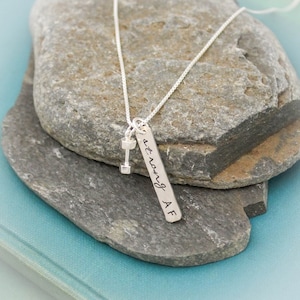 May include: Silver necklace with a dumbbell charm and a rectangular tag that says "strong AF".