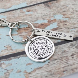 May include: Silver compass keychain with a silver tag that reads "Enjoy the Journey" with an arrow pointing to the right.