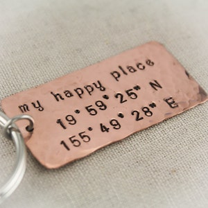 May include: A copper keychain with the text "my happy place" and coordinates 19°59' 25" N 155°49' 28" E.