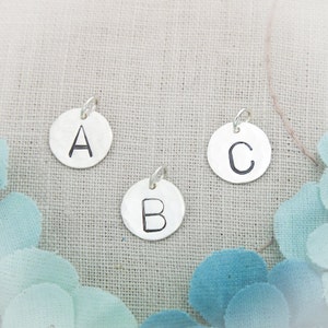May include: Three silver charms with the letters A, B, and C stamped on them. The charms are round and have a slightly hammered texture.