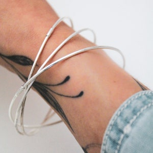 Op de afbeelding: Drie zilveren armbandjes gestapeld op iemands pols.