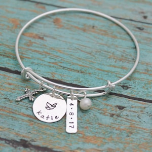 May include: Silver charm bracelet with a cross, a dove, a pearl, and a tag with the text "Katie 4.8.17".