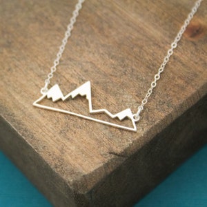 May include: A silver necklace with a mountain range pendant. The pendant is a simple outline of a mountain range.