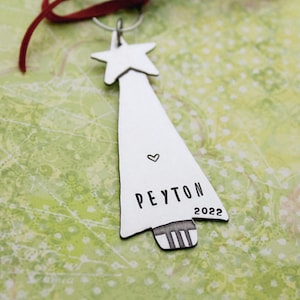 Puede incluir: Un adorno de árbol de Navidad plateado con una estrella en la parte superior, el nombre Peyton y el año 2022 grabados en él.