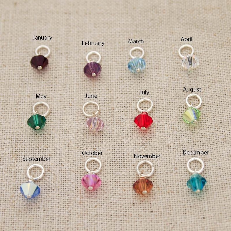 May include: Twelve crystal charms in various colors, each representing a different month of the year. The charms are attached to silver rings.