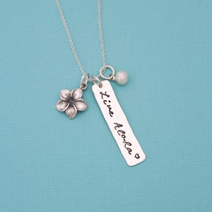 May include: Silver necklace with a small flower charm, a pearl charm, and a rectangular tag that says "Live Aloha" with a heart symbol.