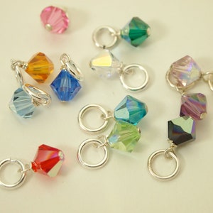 May include: Assortment of colorful crystal beads with silver jump rings. The beads are in various shapes and sizes, including square, round, and teardrop.