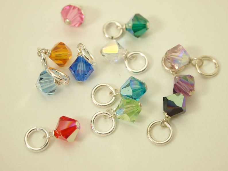 May include: Assortment of colorful crystal beads with silver jump rings. The beads are in various shapes and sizes, including square, round, and teardrop.