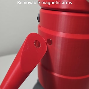 May include: A bright red cylindrical object featuring a detachable arm component. The arm and the main body each contain a circular metal magnet, allowing for connection. The text "Removable magnetic arms" is printed at the top of the image.