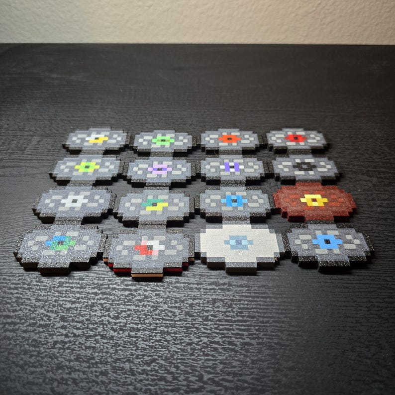 May include: A collection of sixteen square coasters arranged in a four-by-four grid. Each coaster features a pixelated, circular design in the center with varying colors including red, blue, green, yellow, purple, white, and black on a gray background.