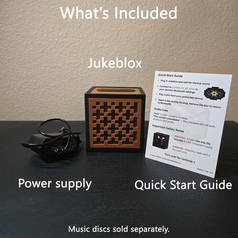 May include: A black and brown square Jukeblox speaker with a geometric cross-patterned front panel, a black power supply unit, and a white Quick Start Guide paper containing instructions, safety notes, and a pixelated disc graphic illustration.