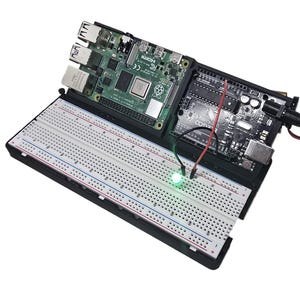 Op de afbeelding: Een groene LED-lamp is aangesloten op een breadboard, dat op zijn beurt is aangesloten op een Raspberry Pi en een Arduino-bord. De Raspberry Pi is aangesloten op een voeding en een netwerkkabel. Het Arduino-bord is aangesloten op een voeding en een USB-kabel.