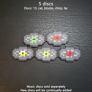May include: Five pixelated music discs with gray circular bodies and distinct colored centers in green, red, yellow, lime, and dark red. Text reads: 5 discs, Discs: 13, cat, blocks, chirp, far, Music discs sold separately, New discs will be continually added.