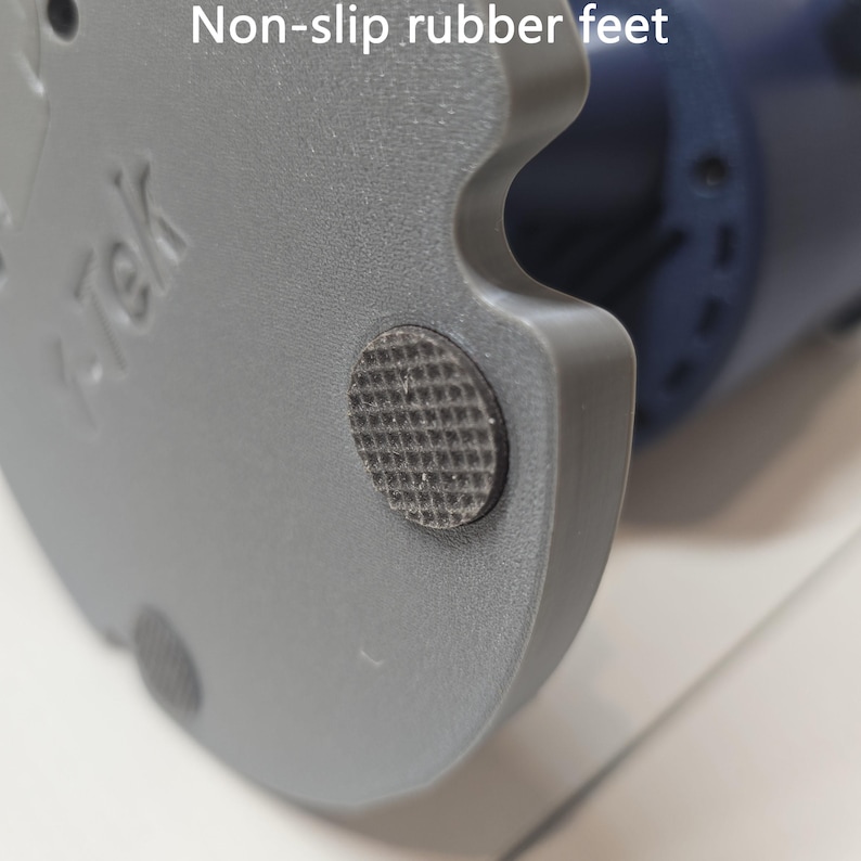 May include: A gray circular base of a device featuring a textured black non-slip rubber foot. The base has a molded gray plastic surface with the embossed text "K-Tek" visible on the side. The design includes a cutout section along the edge.