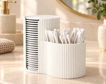 May include: A white ribbed bathroom organizer featuring a vertical stack of round cotton pads on one side and an open compartment filled with white cotton swabs on the other side. The container has a curved, dual-section design.