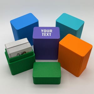 May include: A collection of rectangular, ribbed storage boxes in blue, teal, purple, orange, and green. The purple box features the white text YOUR TEXT. One green box is open, revealing a deck of playing cards with a visible Joker card inside.