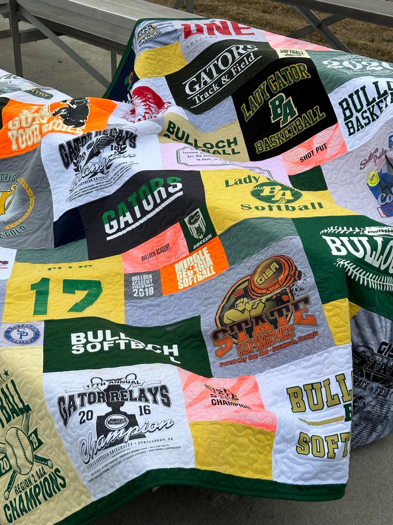 以下が含まれることがあります： 緑、白、黄色のパッチワークキルトは、古いTシャツで作られています。キルトには、「ゲーター」、「バロックアカデミー」、「レディーゲーター」、「ソフトボール」、「ブル」、「ステート」など、さまざまなスポーツチームのロゴと名前が描かれています。