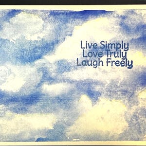 May include: Watercolor painting of a blue sky with white clouds. The words "Live Simply Love Truly Laugh Freely" are written in black on the clouds.