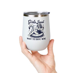 Puede incluir: Un vaso de vino aislado blanco con borde y tapa plateados. El vaso presenta una ilustración en blanco y negro de una mujer en un flotador de flamenco con el texto "Girls Just Want To Have Wine."
