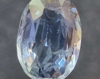 Könnte beinhalten: Ein ovaler, hellblauer Edelstein, der mit einer Pinzette gehalten wird. Der Edelstein ist facettiert und hat eine klare, glasartige Oberfläche.