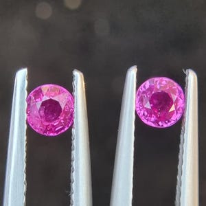 Puede incluir: Dos gemas rosadas se sostienen con pinzas. Las gemas son redondas y tienen un corte facetado.