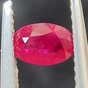 May include: A vibrant red oval-shaped gemstone held in a pair of silver tweezers.
