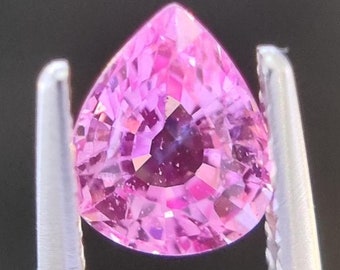 May include: A pink pear-shaped gemstone with a faceted cut, held in tweezers.