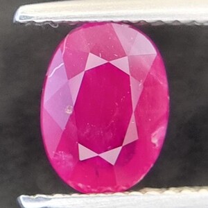 Pode incluir: Uma gema de rubi ovalada de cor rosa vibrante, segurada por uma pinça.