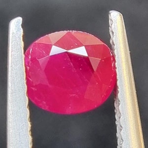 Pode incluir: Uma gema de rubi vermelho brilhante com corte facetado, segurada em uma pinça.