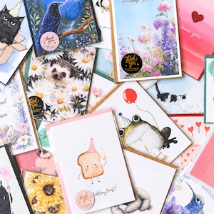 Peut inclure: Une collection de cartes de v&oelig;ux avec diverses illustrations. Les motifs comprennent un chat noir, un oiseau bleu, un h&eacute;risson, une grenouille avec un chapeau de f&ecirc;te et une tranche de pain grill&eacute; avec un chapeau de f&ecirc;te. Certaines cartes portent l'inscription "Happy Birthday" et "love you".