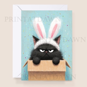 May include: Greeting card featuring a grumpy black cat wearing bunny ears, peeking out of a cardboard box. The background is light blue with colorful confetti. The card is inside a white envelope.