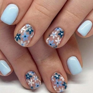Könnte beinhalten: Nahaufnahme von kurzen, hellblauen Nägeln mit einem transparenten Blumendesign. Die Blumen sind weiß mit blauen Zentren.