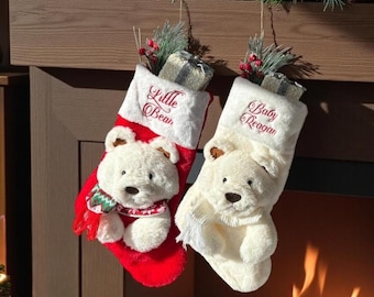 Op de afbeelding: Twee kerstsokken met pluche witte berengezichten. De linker sok is rood met een witte boord geborduurd met Little Bear. De rechter is wit met een boord geborduurd met Baby Reagan. Beide zijn versierd met groen en bessen.