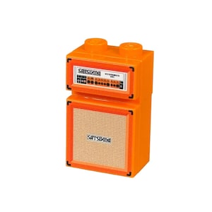 May include: A bright orange toy amplifier featuring the text "SATSUKIDA" on the speaker and control panel. The speaker has a beige mesh cover. The control panel displays lights and knobs. It's a miniature replica of a Rockbrick MKII.