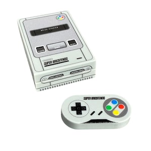 Peut inclure: Un ensemble console et manette Super Bricktendo blanc et gris. La console porte l'inscription "BRICK VERSION" et "SUPER BRICKTENDO". La manette comporte une croix directionnelle et des boutons colorés.