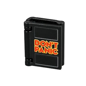 May include: A black, hinged book with the words "DON'T PANIC" in orange and yellow lettering. The book is rectangular with rounded corners and a visible spine. The text is centered on the front cover.