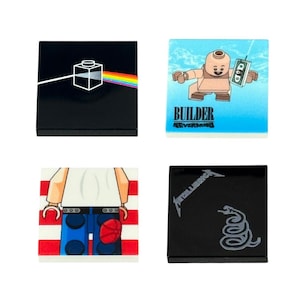 Op de afbeelding: Vier vierkante Lego-tegels met unieke ontwerpen. Eén tegel toont het Pink Floyd prisma-logo, een andere heeft een Lego-figuur met de tekst "BUILDER NEVERMIND", een derde toont een figuur met een Amerikaans vlagontwerp en de laatste heeft het Metallica-logo.