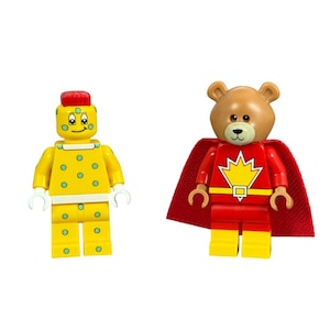 May include: Two Lego figures: a yellow character with blue dots and a red-topped head, and a bear figure in a red superhero outfit with a yellow emblem and a red cape. Both figures have white hands.