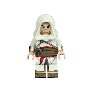 Peut inclure: Une figurine Lego d'un personnage vêtu d'une robe à capuche blanche avec une ceinture marron et une écharpe rouge. La figurine a une expression sévère et une courte barbe. La figurine porte une capuche blanche et une ceinture marron avec des pochettes.