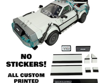 May include: A white and gray building block model of a sports car with translucent blue accents, a black antenna, and black wheels. Beside the car are several custom printed white and black rectangular building block pieces and tiles.