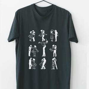 May include: Dark gray t-shirt featuring a white graphic of couples dancing in various poses. The design includes nine different illustrations of couples in motion, with a simple, minimalist style. The shirt is hanging on a black hanger.