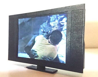 Op de afbeelding: Een zwarte televisie met een scherm dat een scène uit een film laat zien. De scène toont een wezen dat een persoon in zijn armen houdt.