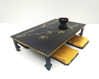 May include: A black lacquered table with gold bamboo design and two gold cushions. The table has four legs and a small black bowl on top.