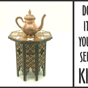 Può includere: Un tavolo di legno con intagli intricati e una teiera di rame in cima. Il tavolo ha un motivo geometrico bianco e marrone sulla parte superiore. Il testo "DO IT YOURSELF KIT" è visibile nell'immagine.