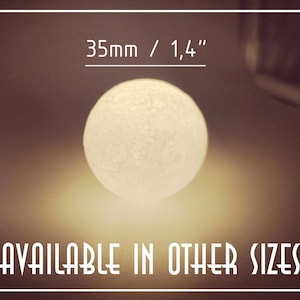 Op de afbeelding: Een getextureerde witte bol, met een diameter van 3,5 cm, straalt zachtjes. De afbeelding bevat de tekst "AVAILABLE IN OTHER SIZES". De bol wordt verlicht tegen een warme bruine achtergrond. De bol is ongeveer 1,4 inch in diameter.
