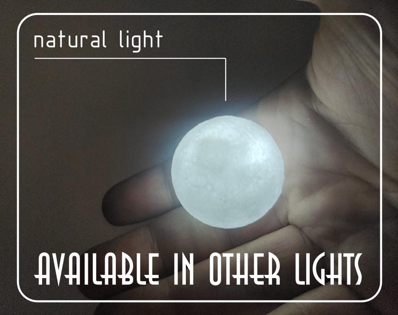 Op de afbeelding: Een gloeiende, bolvormige lichtbron, die lijkt op een kleine maan, in een hand gehouden. De tekst "natural light" en "AVAILABLE IN OTHER LIGHTS" zijn in het wit weergegeven. Het licht straalt zacht wit.