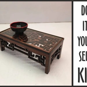 Peut inclure: Une table en bois avec un plateau en verre et des découpes complexes. La table est brune et a un bol noir sur le dessus. Le texte "DO IT YOURSELF KIT" est visible en arrière-plan.